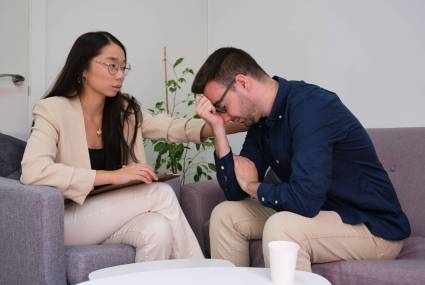 Asian female psychologist comforting caucasian man patient at therapy. Mental health concept.