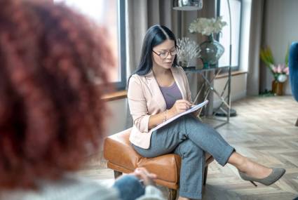 Asian stylish psychoanalyst. Asian stylish psychoanalyst writing down notes while listening to client