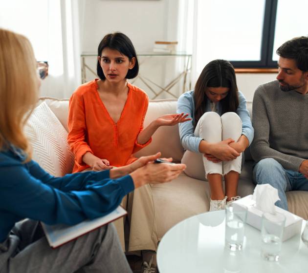 Upset teenager girl with her parents at a psychologist's appointment. Family at psychology session. Psychologist helping young family with a child to solve teenagers problems.