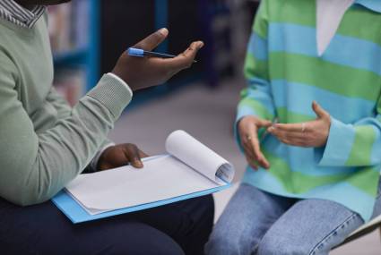 Side view closeup of male therapist holding clipboard and gesturing during support session with teenage girl