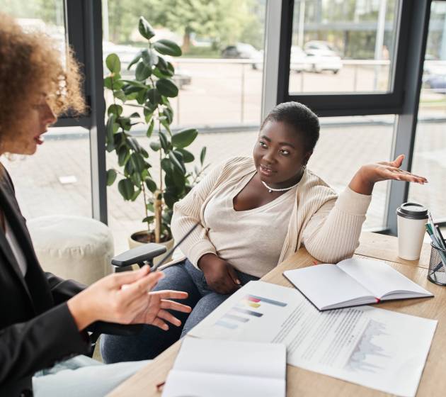 curvy african american businesswoman talking to colleague near documents with graphs in office