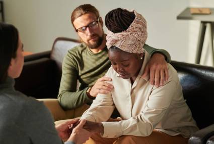 Woman in depression visiting psychologist together with her husband, they supporting her during session