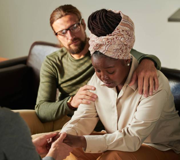 Woman in depression visiting psychologist together with her husband, they supporting her during session