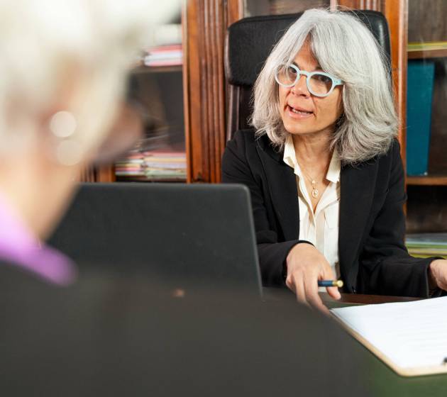 A senior female lawyer - consulting with a client across the desk - professional legal environment, focus on experience and trust, attorney-client discussion, mature legal advisor woman at work.