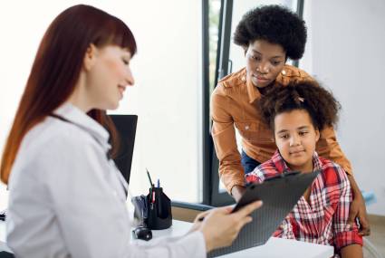 Female doctor pediatrician showing medical report or medical test results to young African mother and her tenn daughter on a clipboard in modern clinic. Children doctor talking to patient
