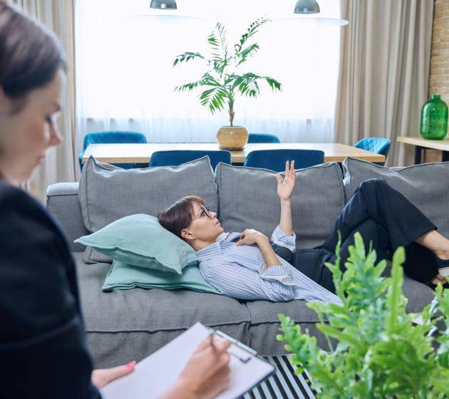 Female psychologist is having therapy session with middle-aged woman patient lying on sofa in office. Psychology, psychotherapy, therapy, counseling, treatment, mental health concept