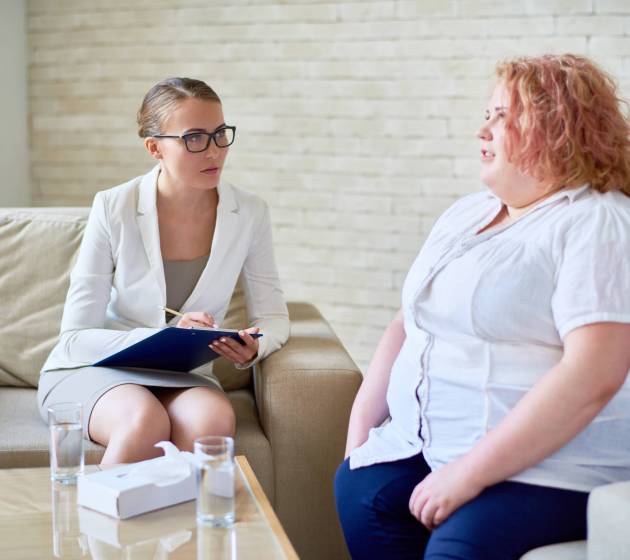 Portrait of obese young woman opening up to female psychiatrist during therapy session  on mental issues