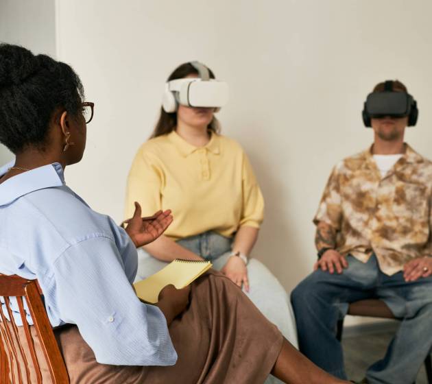 Three people engaging virtual reality experience in education setting with headsets while sitting in chairs, each exploring various applications and environments in immersive learning