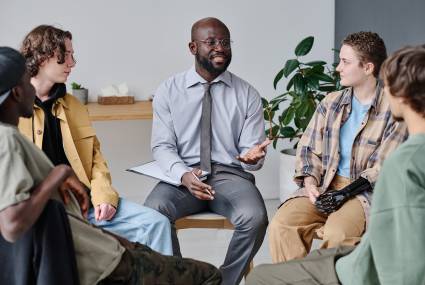 African psychotherapist talking to young people during session at class