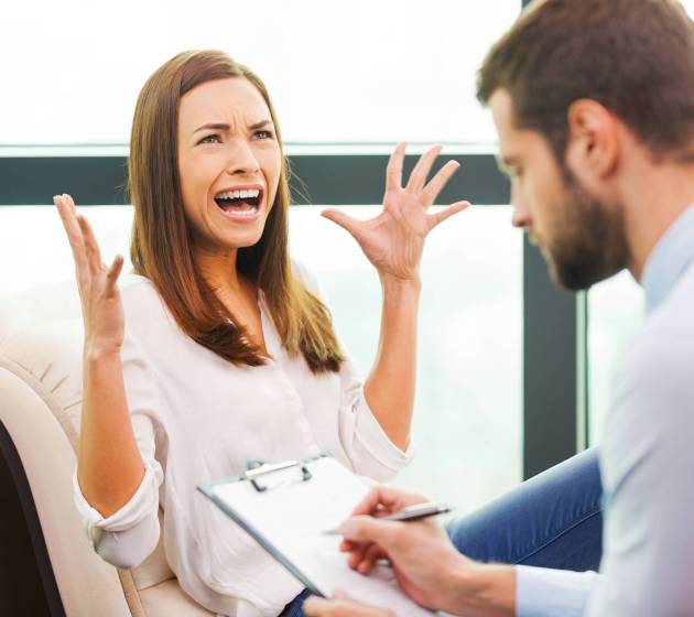 She needs an expert advice. Depressed young woman sitting at the chair and holding hand on head while young man sitting close to her and writing something in his clipboard