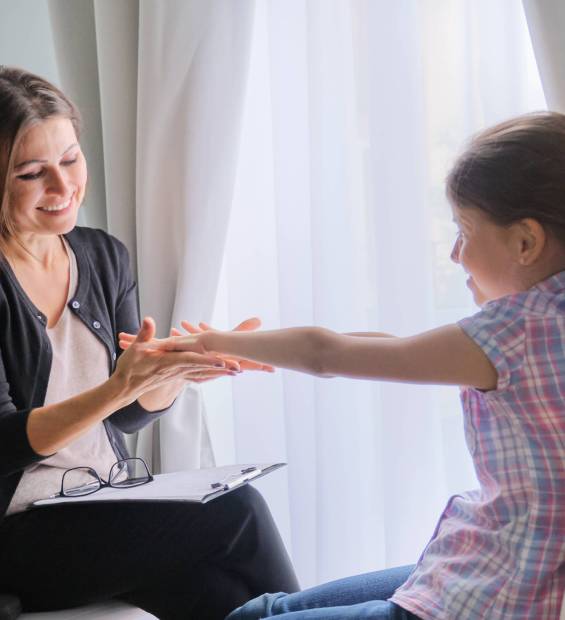 Talking girl and woman psychotherapist in office near window. Child psychology, mental health
