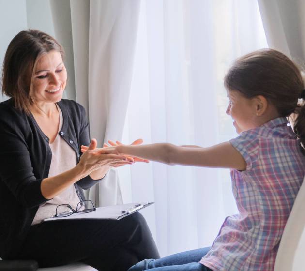 Talking girl and woman psychotherapist in office near window. Child psychology, mental health