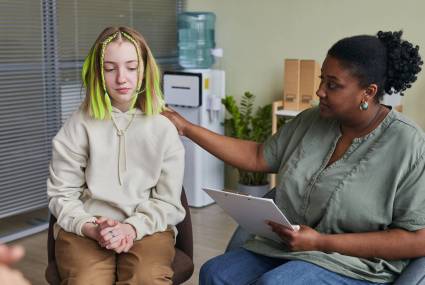 Teenage girl sitting on chair and talking with specialist giving her an advice during therapy class