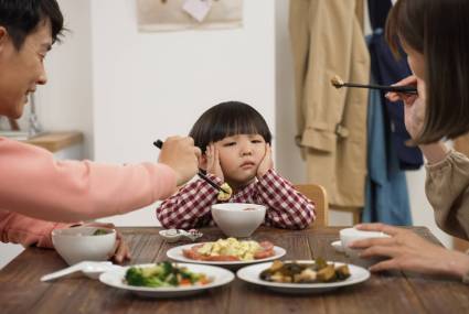 closeup of unhappy Asian preschool boy shaking head and saying no to eat at dining table to his mom and dad at home
