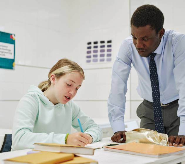 Portrait of young black teacher helping teenage girl in school classroom